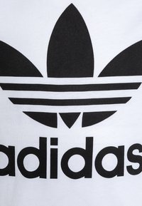 Logo trefoil Adidas nero con tre strisce su sfondo bianco di cotone. Il design è audace e prominente, caratterizzato da una texture liscia.