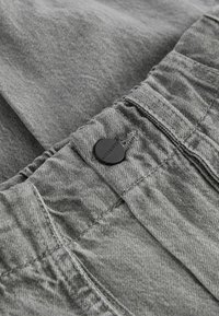 Grijs denim stof met een gestructureerde afwerking en een elastische tailleband, voorzien van een zwarte ALLSAINTS logo knoop aan de voorkant.