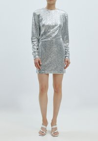 Silberner Paillettenkleid mit langen Ärmeln, tailliertem Design, rundem Ausschnitt und Mini-Länge. Getragen mit weißen Riemchenheels.