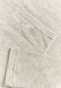 Camicia a maniche lunghe grigia chiaro realizzata in tessuto morbido, con collo e orlo cuciti, e un'etichetta che fornisce istruzioni per la cura.