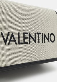 Valentino bag featuring a textured beige surface with black logo lettering, accented by black edges and stitching. Rectangular shape.