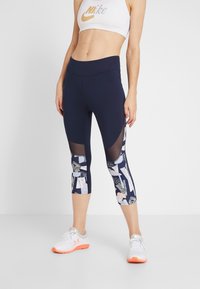 Los leggings capri en color navy cuentan con un panel de malla y un diseño abstracto colorido en las piernas inferiores. Están hechos de un tejido elástico y transpirable.