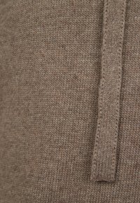 Brown knitted fabric with a ribbed texture and a vertical contour. Features a prominent strand along one edge, highlighting the pattern.