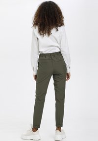 khaki tapered broek met een rekbare tailleband, twee achterzakken en opgerolde mouwen. Gecombineerd met een witte langemouwen shirt en sneakers.