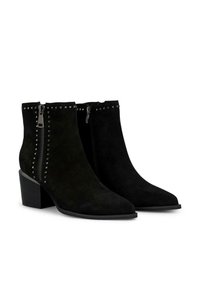 Botas de tobillo de ante negro con puntera afilada, acentos de tachuelas plateadas a lo largo del zipper y un tacón apilado para mayor altura.