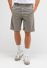 Grijze katoenen shorts met een elastische tailleband, twee zijzakken en een knoopsluiting. Geloofd met witte sokken en grijze schoenen.
