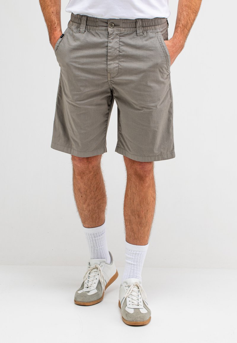 Grijze katoenen shorts met een elastische tailleband, twee zijzakken en een knoopsluiting. Geloofd met witte sokken en grijze schoenen.