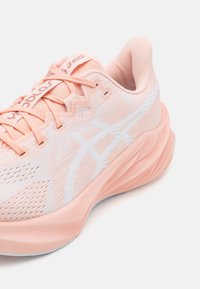 Light pink athletic shoe with a textured mesh upper, white accents, and a cushioned, ridged sole. Features sturdy laces and branding.