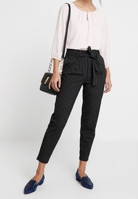 Ljusrosa blus med samlad halsringning, svartvita randiga högmidjade byxor med knutet bälte, blå loafers och en svart handväska.