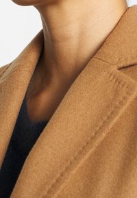 Bruin wollen mix jas met een zachte textuur. Het kledingstuk heeft een geknipt revers en subtiele stikseldetails.