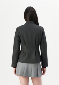 Chaqueta gris ajustada con un cuello alto y corte estructurado, combinada con una falda gris con plisados, que exhibe texturas suaves y líneas limpias.