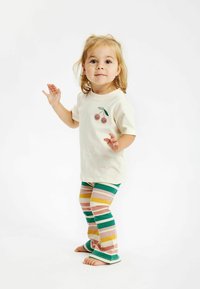 Krämfärgad t-shirt med körsbärsgrafik, kombinerad med flerfärgade randiga leggings i grönt, rosa och gult; båda i mjukt, stretchigt tyg.