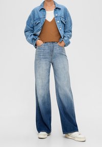 Ljusblå denimjacka med blommönster, ihopparad med en brun ribbad linne och högmidjade vida jeans. Vita sneakers.