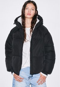 Černá péřová bunda s vysokým límcem a kapucí. Obsahuje prošívaný design, kapsy na zip a stahovací lem. Nositelná přes světlý top.