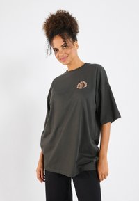 Donkergroen oversized t-shirt met korte mouwen, voorzien van een kleine ronde graphic in oranje op de linkerkant van de borst. Zacht katoenmateriaal.