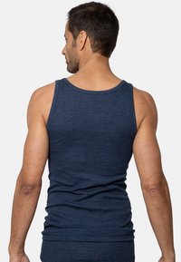 Uomo di spalle che indossa una canotta attillata blu scuro su uno sfondo chiaro e uniforme.