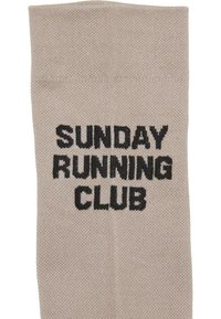 Tessuto a maglia beige con testo nero che recita "SUNDAY RUNNING CLUB" centrato sulla superficie.