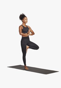 Completo da yoga nero composto da un top aderente e leggings, con un design texturizzato, indossato da una persona che esegue una postura di equilibrio su un tappetino.