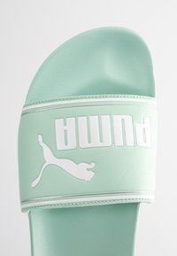 Des claquettes vert clair en matériau synthétique lisse. Présentent un logo blanc avec un silhouette de puma, un design plat et aucun matériel visible.