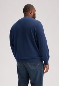 Navy blue sweatshirt with long sleeves, ribbed cuffs, and a relaxed fit. Dark denim jeans with a classic five-pocket design.