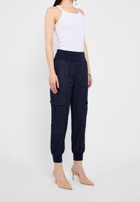 Pantalones cargo azul marino con una cintura elástica y puños ajustados, con bolsillos laterales y un aspecto de denim texturizado, combinados con una camiseta sin mangas blanca.
