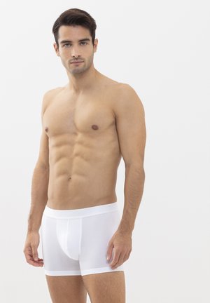 Weiße Baumwoll-Boxershorts mit einem weichen Bund, enganliegendem Design und glatter Textur. Keine Muster oder Logos sichtbar. Modell steht.