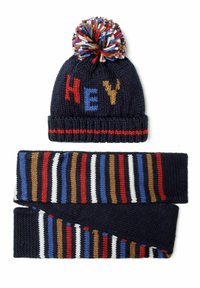 Bonnet tricoté bleu marine avec l'inscription colorée "HEY" et un pompon multicolore ; l'écharpe assortie présente des rayures horizontales dans diverses couleurs.