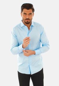 Camicia azzurra a maniche lunghe con colletto, design aderente e texture sottile. Presenta bottoni bianchi e polsini a contrasto.
