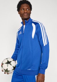 Μπλε αθλητικό μπουφάν με φερμουάρ και λευκές ρίγες, κατασκευασμένο από ελαφρύ υλικό. Διαθέτει πλαϊνές τσέπες και ετικέτα "CLIMACOOL" στο τελείωμα.