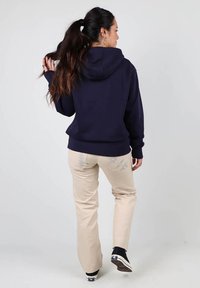 Haut à capuche bleu marine avec une poche kangourou, associé à un pantalon beige avec un motif décoratif à l'arrière. Des baskets noires complètent le look.