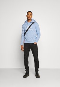 Felpa blu chiaro con logo bianco, pantaloni neri in stile jogger e stivaletti neri alla caviglia. La felpa presenta una tasca frontale e lacci.