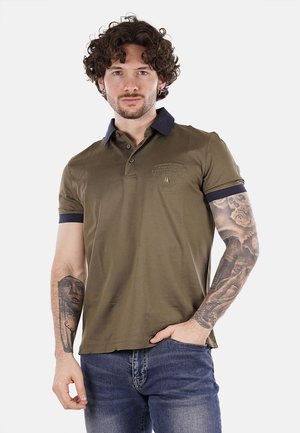 Polo verde oliva con colletto e polsini blu navy, maniche corte e dettaglio del logo sul petto, abbinato a jeans in denim.