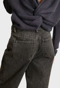 Jeans negros de cintura alta con un diseño de pierna recta, textura sutil y bolsillos traseros con parche. Combinados con un suéter de punto oscuro.