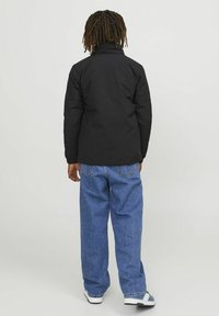 Svart puffjacka med hög krage, tillsammans med löst sittande blå jeans. Outfiten har en texturerad tyg och minimala detaljer.