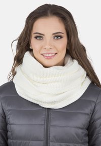 Tyk hvid strikket infinity-scarf lagd over en mørk dunjakke, med et struktureret væv for ekstra varme og komfort.