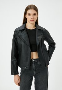 Zwarte faux leren motorjack met een asymmetrische rits, spitse kraag en ritszakken aan de voorkant. Gestyled met een cropped zwarte top en jeans.