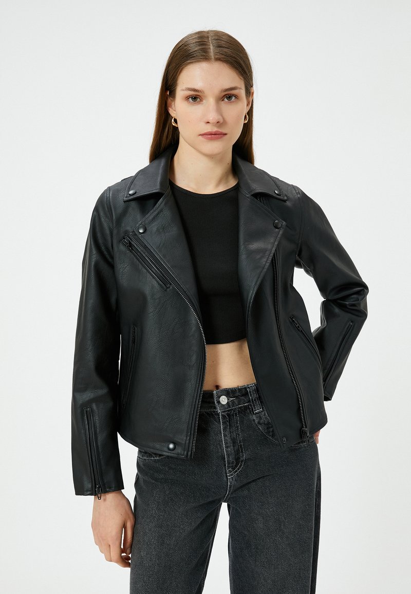 Zwarte faux leren motorjack met een asymmetrische rits, spitse kraag en ritszakken aan de voorkant. Gestyled met een cropped zwarte top en jeans.