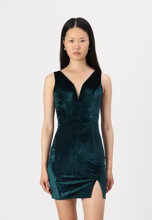 Robe en velours vert avec un décolleté en V profond, design ajusté et une fente haute sur un côté. Texture lisse, style sans manches.