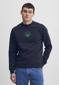 Mørkeblå hettegenser med grønn "CASUAL FRIDAY"-tekstlogo på brystet, ribbestrikket rund hals og mansjetter, laget av mykt bomullsmateriale.