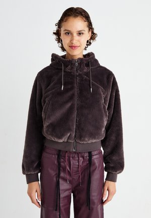 Haut à capuche cropped gris foncé duveteux avec une fermeture éclair à l'avant, une capuche et une taille élastique. Il présente des cordons de serrage et un tissu doux et texturé.