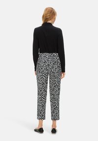 Schwarzes Langarmoberteil, kombiniert mit einer locker sitzenden Hose mit monochromem Leopardenmuster, glattem Stoff und knöchellanger, verkürzter Passform.