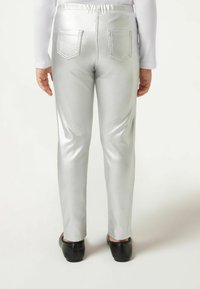 Silberne metallische Leggings mit glänzender Textur, ausgestattet mit zwei Gesäßtaschen und einem figurbetonten Design, kombiniert mit schwarzen Ballerinas.
