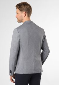 Grau gewobener Blazer mit Reverskragen, einfacher Schlitzen und zwei Knopfüffnungen. Strukturierter Stoff mit dezentem Muster und taillierter Passform.