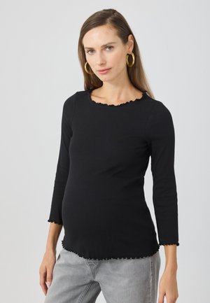 Black ribbed long-sleeve shirt with a scalloped neckline and hem, featuring a fitted silhouette and soft texture, paired with gray pants.