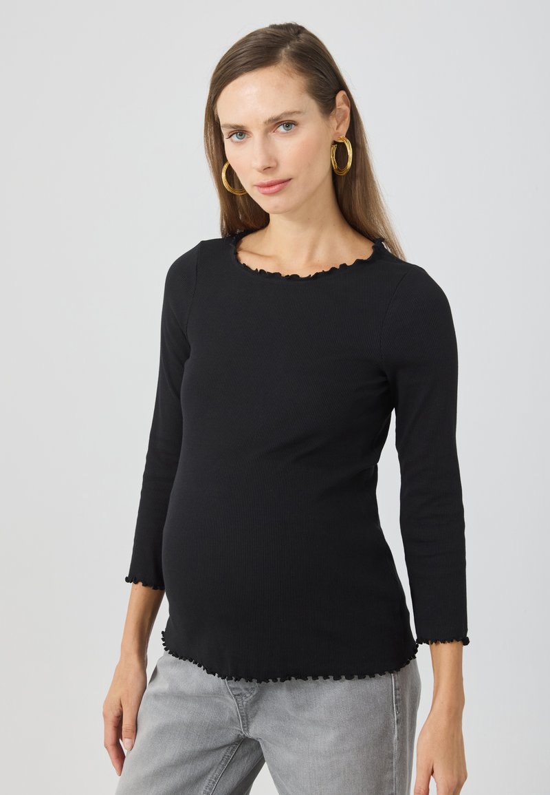 Black ribbed long-sleeve shirt with a scalloped neckline and hem, featuring a fitted silhouette and soft texture, paired with gray pants.
