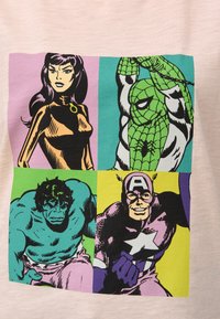 T-paita, jossa on sarjakuvamainen printti: neljä hahmoa erivärisissä lohkoissa—violetissa, vihreässä, vaaleanpunaisessa ja keltaisessa—vaaleanpunaisella taustalla.