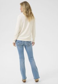 Top a maniche lunghe di colore crema abbinato a jeans a zampa d'elefante di colore blu chiaro. I jeans presentano cuciture decorative sui taschini posteriori e una vestibilità slim.