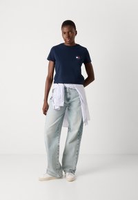 Marineblå bomulds T-shirt med et lille logo på brystet, parret med lys blå brede jeans og en stribet skjorte bundet om taljen.