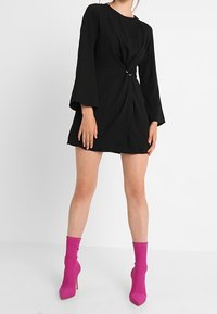 Svart klänning med en knutdetalj i midjan och långa klockärmar. Bärs med klarröda anklarstövlar som har en slät, glansig yta.