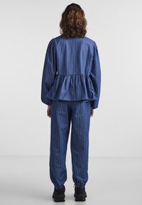 Μπλε ριγέ τοπ με peplum και φουσκωτά μανίκια, συνδυασμένο με χαλαρές παντελόνες στο ίδιο σχέδιο, και τα δύο φτιαγμένα από μαλακό ύφασμα με ελαφρώς υφασμένη επιφάνεια.